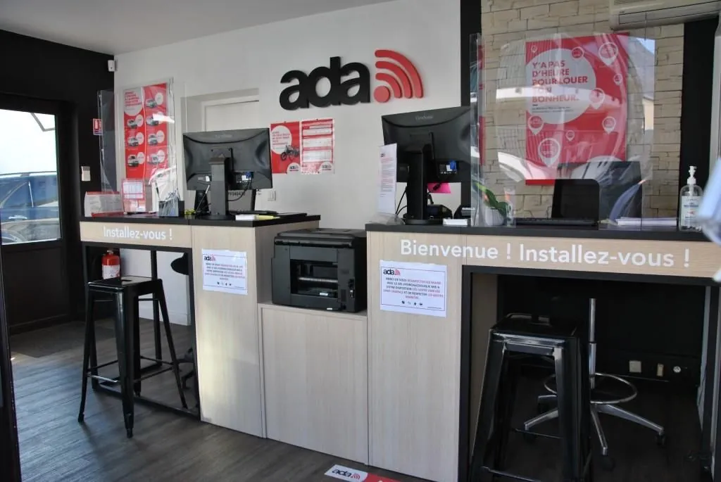 Comptoir d'accueil d'une agence ADA équipé de deux postes informatiques, avec des tabourets pour les clients